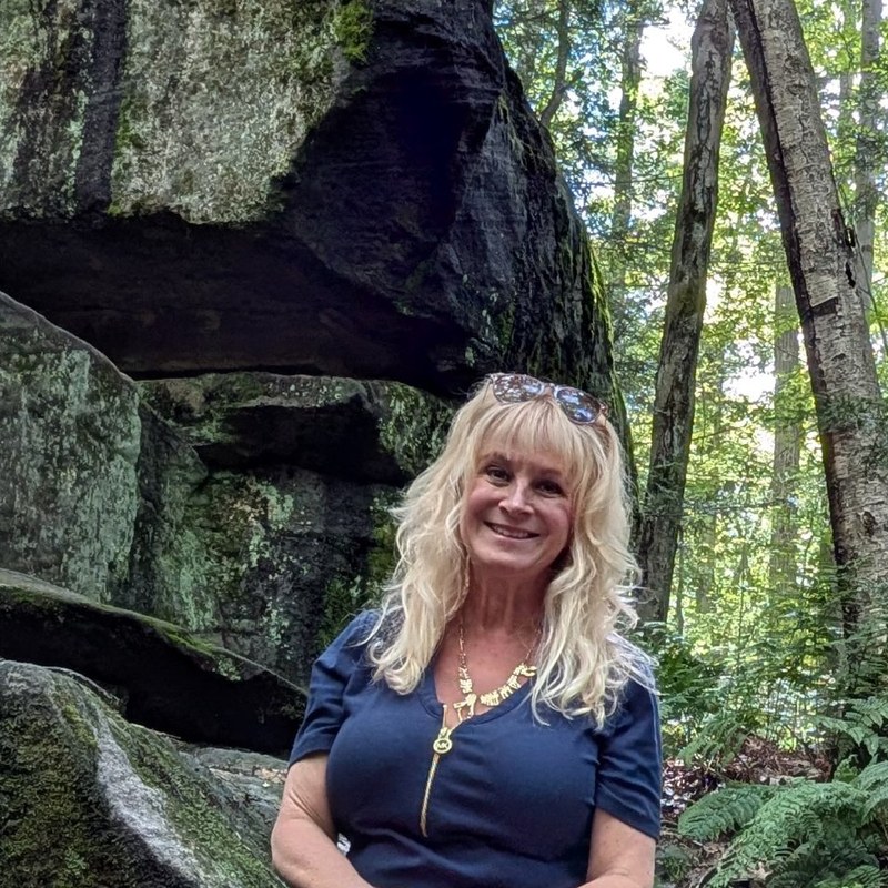 Lora Stefanowicz, White Coat captioner, sitting on mossy boulders in the forest